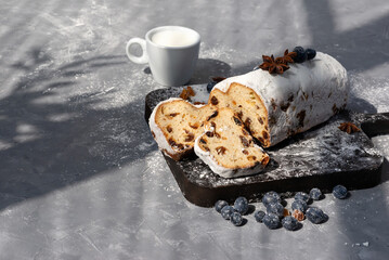 Sliced stollen with raisins and blueberry on wooden board, cup of milk, aesthetic sunlight shadows...