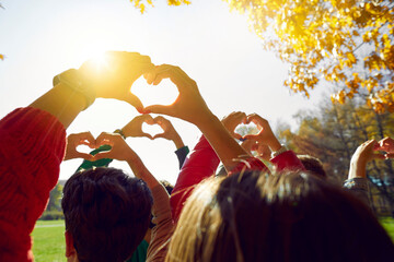 Group of friends making heart shapes with their hands against sunset. Young people walking in park...