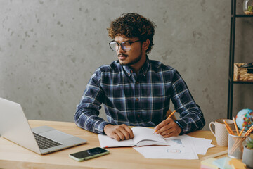 Successful minded pensive employee business Indian man he wearing casual blue checkered shirt...