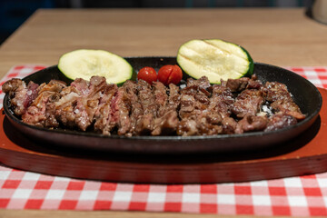 close-up detail of a lightly grilled fillet of veal with vegetables and coarse salt, served on a ceramic plate on a red and white checkered tablecloth.