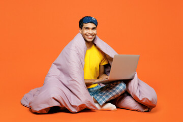 Full body young IT man wear pyjamas jam sleep eye mask sit wrapped in duvet rest relax at home work...