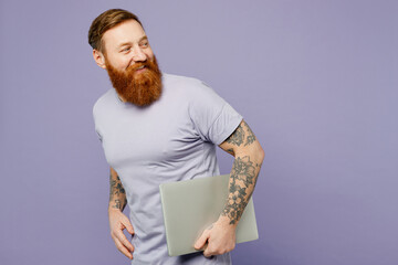 Side view young happy redhead bearded IT man wearing violet t-shirt casual clothes hold closed...