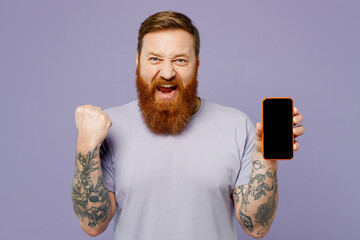 Young redhead bearded man wearing violet t-shirt casual clothes hold in hand use mobile cell phone...