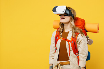 Young woman carry backpack with stuff mat watching in vr headset pc gadget isolated on plain yellow...