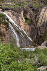 vertical image of the tree-filled mountain waterfall in the foreground of the Ézaro in Dumbria, La Coruña, Galicia, Spain
