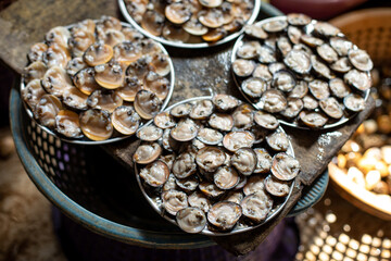 Opened small oysters sold at market in India. Slippery mussels lie on four similar plates at...