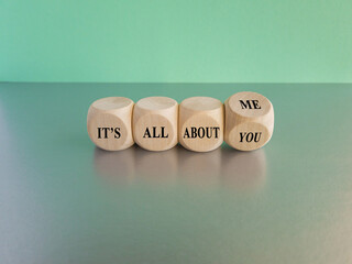 Hand turns dice and changes the expression 'it's all about you' to 'it's all about me'. Beautiful grey table, blue background. Copy space.