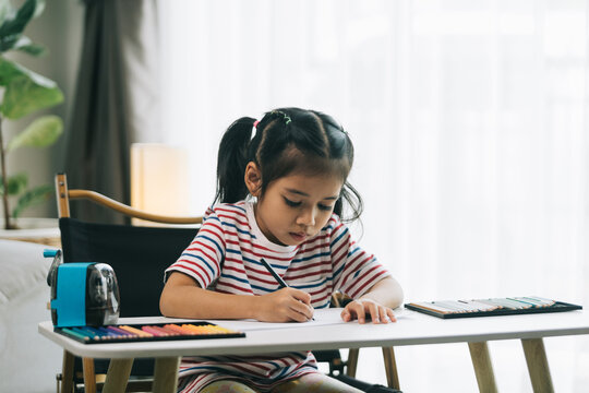 Little asian girl drawing with pencils in living room at home