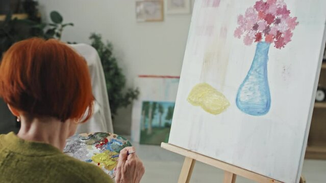 Handshake of senior woman sitting in front of canvas drawing still life picture in cozy room at daytime