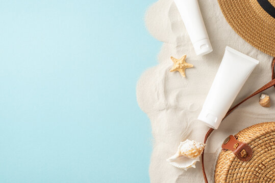 Set stage for sun protection with top view arrangement of SPF cream tubes, purse, sunhat, seashells, starfish, palm leaf on pastel blue and sandy background. Empty space invites text or advertising