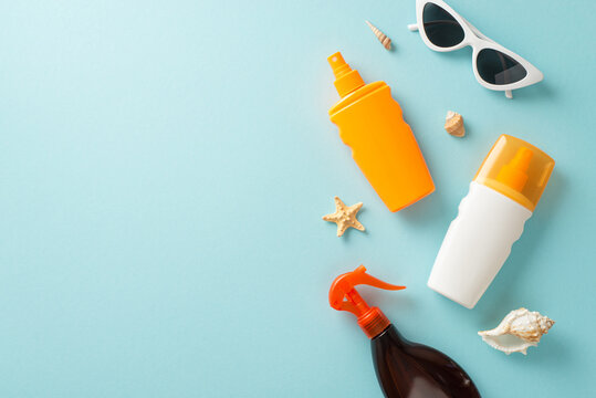 Sun protection collection. Blank space for branding on a pastel blue background featuring top view of sunblock oil and SPF cream bottles without labels, sunglasses, shells, and starfish