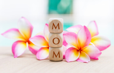 Mom text on wooden cube with beautiful plumeria flower, mother's day card background idea