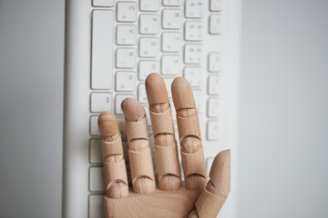 木製のロボットの手の指とパソコンのキーボード