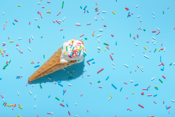 top view of ice cream cone and strewed sprinkles on blue with hard shadow, summer concept