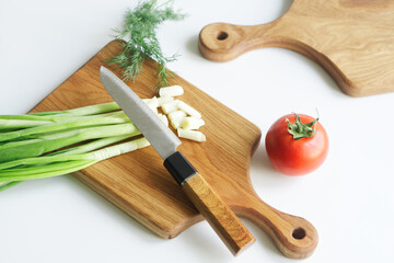 Sharp knife, chopped green onion, vintage solid oak wooden cutting boards and fresh tomato on a light background. Concept of cooking a rustic summer vegetable salad. Photo. Selective focus.