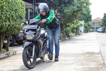 Asian online taxi driver in green jacket do a kick starter to start the motorbike 