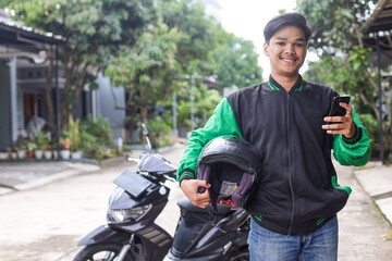 Portrait of Asian online taxi driver wearing green jacket holding helmet and smartphone
