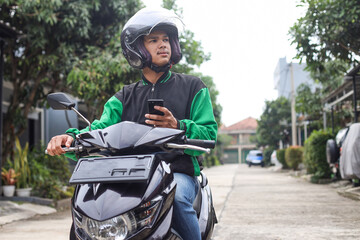 Asian man work as a commercial motorcyle taxi driver taking order and looking for customer address from his smartphone