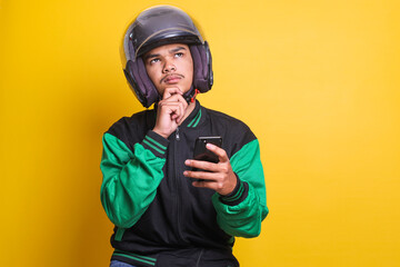 Asian online taxi driver wearing green jacket and helmet using mobile phone while thinking and looking to the upper side