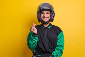 Asian online taxi driver wearing green jacket and helmet showing heart sign over yellow background