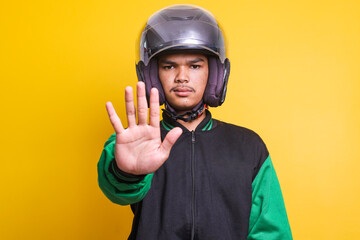 Asian online taxi driver wearing green jacket and helmet showing no hand sign, gesturing warning or...