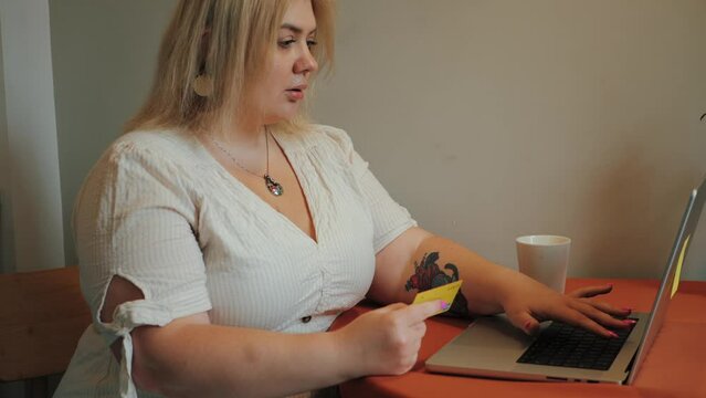 Plus size woman typing credit card details in laptop, doing online shopping, making purchase.