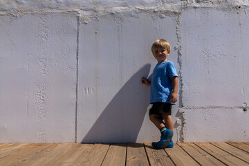boy 3 years old blond blue t-shirt black shorts stands against the background of a white wall Fashion photography