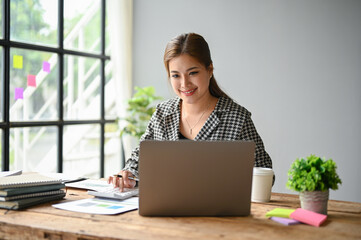 A businesswoman sits at her desk in her office and focuses on her work on her laptop.