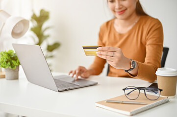 A woman sits at a table, holding a credit card and using her laptop