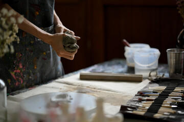 Close-up image of a master clay artist or potter kneading raw clay at his desk