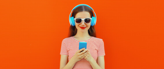 Portrait of smiling young woman in headphones listening to music with smartphone on orange background