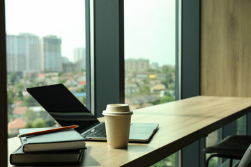 Office table by the window with coffee, laptop and notebooks