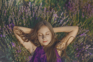 Young pretty girl in violet dress lying with closed eyes in lavender field among flowers in Provence, sleeping or dreaming at sunset, outdoor lifestyle  evening portrait, idea of relax and summer vibe