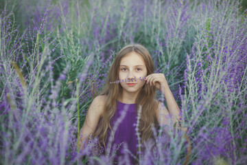 Young pretty smiling girl teen in violet dress sitting in lavender field in Provence and smelling a flower, outdoor child portrait, concept of beauty, happiness, summer vibe, lifestyle in countryside