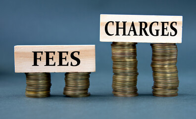 FEES CHARGES - words on a wooden block against the background of stacks of coins