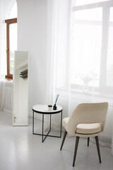 White interior fashionable armchair chair with coffee table, mirror with white curtains. Modern interior, vertical photo. 