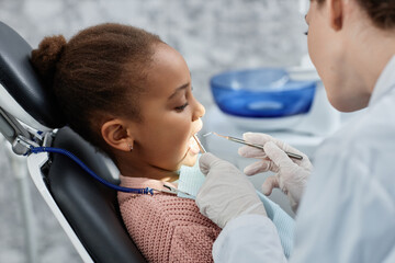 Side view portrait of black little girl in dental chair during teeth checkup with dentist pediatrician, copy space