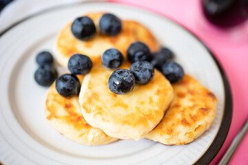 Close-up of golden toasted syrniki or cottage cheese with blueberries on a white plate. Homemade cooking. Sweet and delicious breakfast
