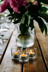 Burning candles in a glass glass on a background of flowers.