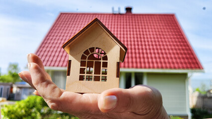 Small wooden toy house on palm of woman hand and big home on background. symbol and concept of cconstruction, buying, selling, donating of eco friendly home. copy space. close-up, soft selective focus