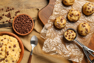 Fototapeta premium Bowl with dough and uncooked chocolate chip cookies on wooden table, flat lay