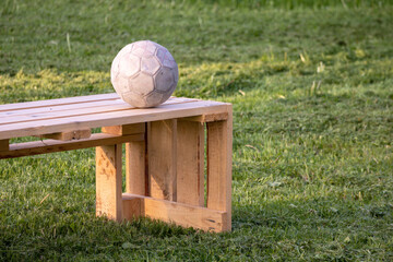 
A bench of pine wood planks is placed on green grass and a white ball is placed on it