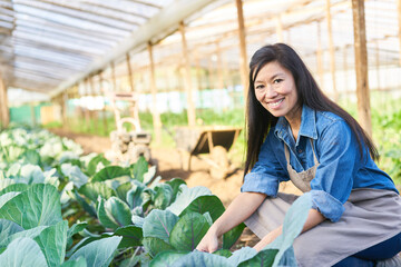 Happy female farmer crouching by fresh plants in farm
