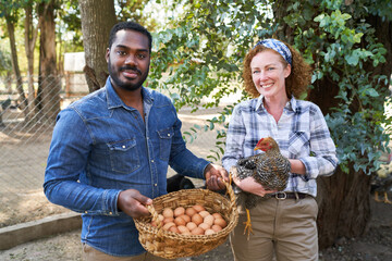 Farmers with eggs and chicken standing in poultry farm