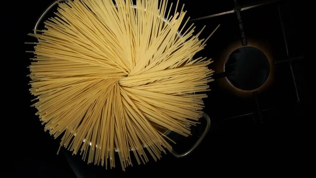 Female  hand of chef throwing spaghetti pasta into silver pot on kitchen stove, top view. 