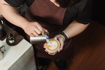Fototapeta na wymiar Top view, Barista pouring milk foam to making latte art coffee. Young man barista working at coffee shop. Latte art menu coffee, Espresso, Coffee menu making concept. Selective focus.