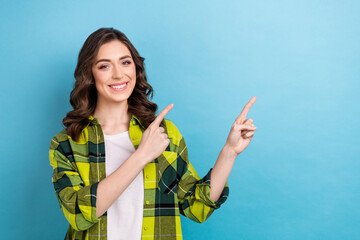 Portrait of cheerful pretty girl wavy hairstyle wear plaid jacket indicating at discount empty space isolated on blue color background