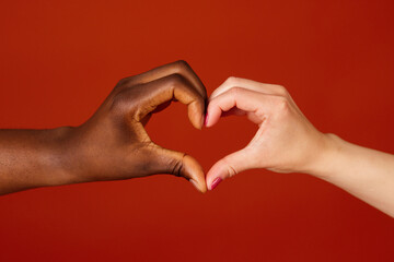 Black and white hands forming heart shape together isolated on  orange background. Close up.