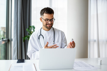 Young doctor speaks with patient using laptop online video webinar consultation sitting in clinic office. Telemedicine. Doctor therapist has a video call conference with a patient