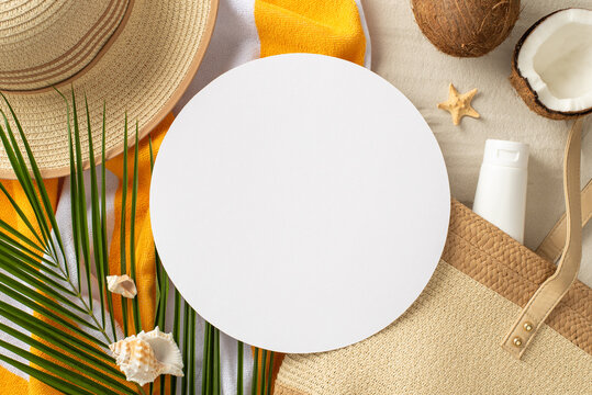Summer vacation concept. Top view photo of empty circle with straw bag and hat, beach towel, palm leaf, coconut, tube sunscreen and shells with starfish on isolated sand background with copyspace